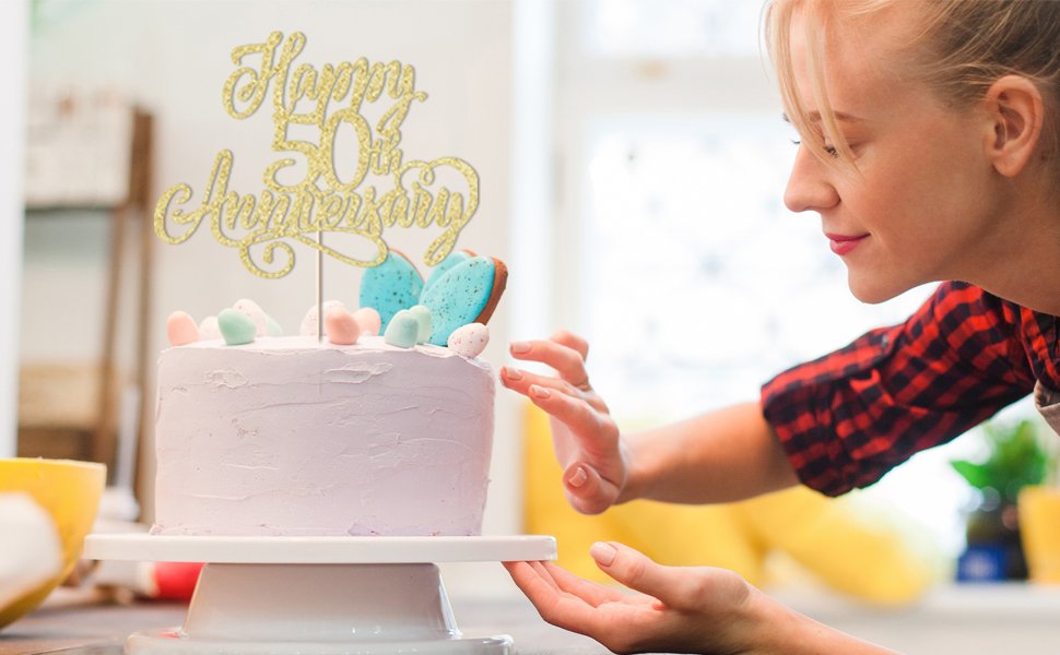Golden glitter cake topper reading 'Happy 50th Anniversary' on a pastel purple cake with decorative cookies and candies.