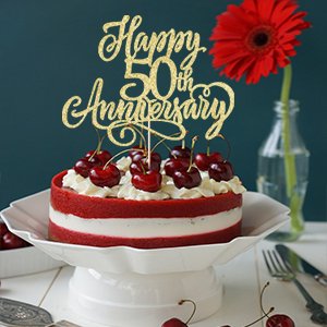 Golden glitter 'Happy 50th Anniversary' cake topper on a red velvet cake with cherries and whipped cream.