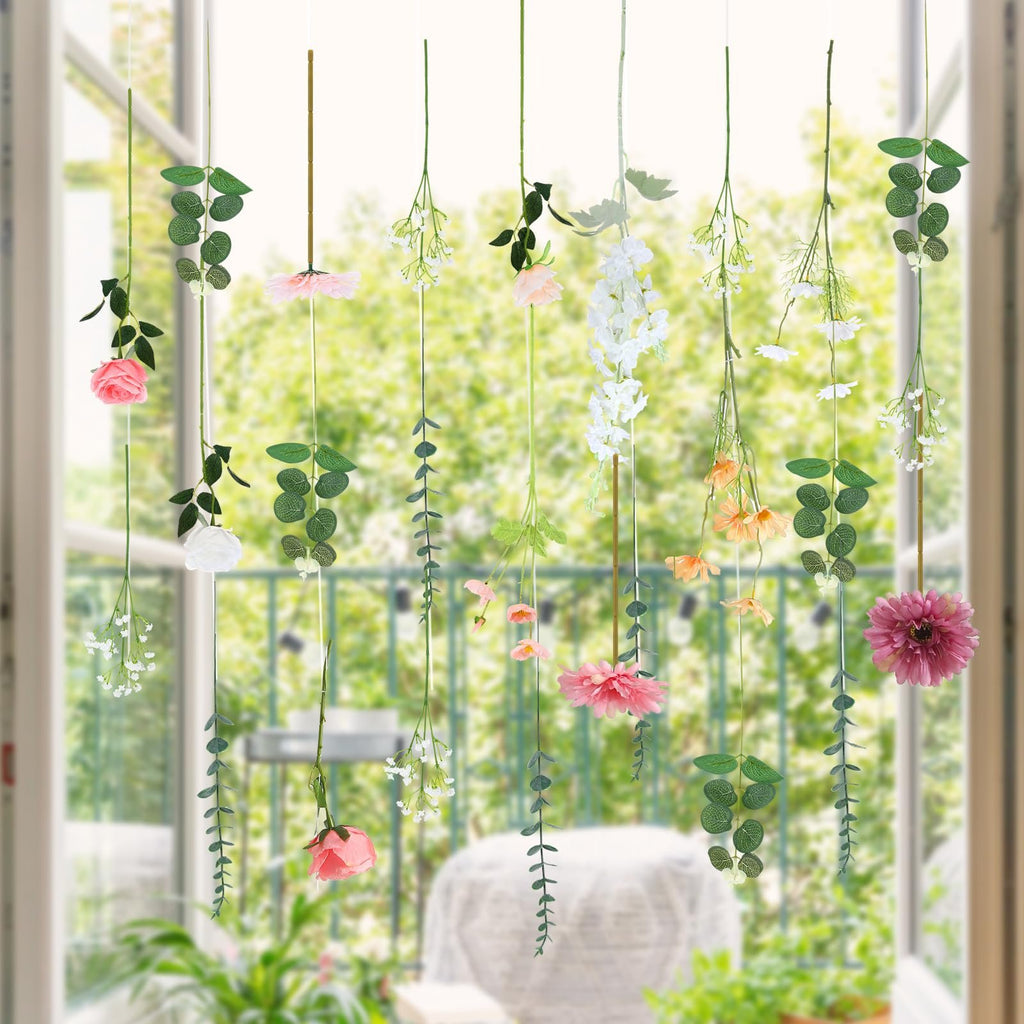 Hanging artificial flowers and greenery in various colors, displayed indoors with a blurred outdoor view.