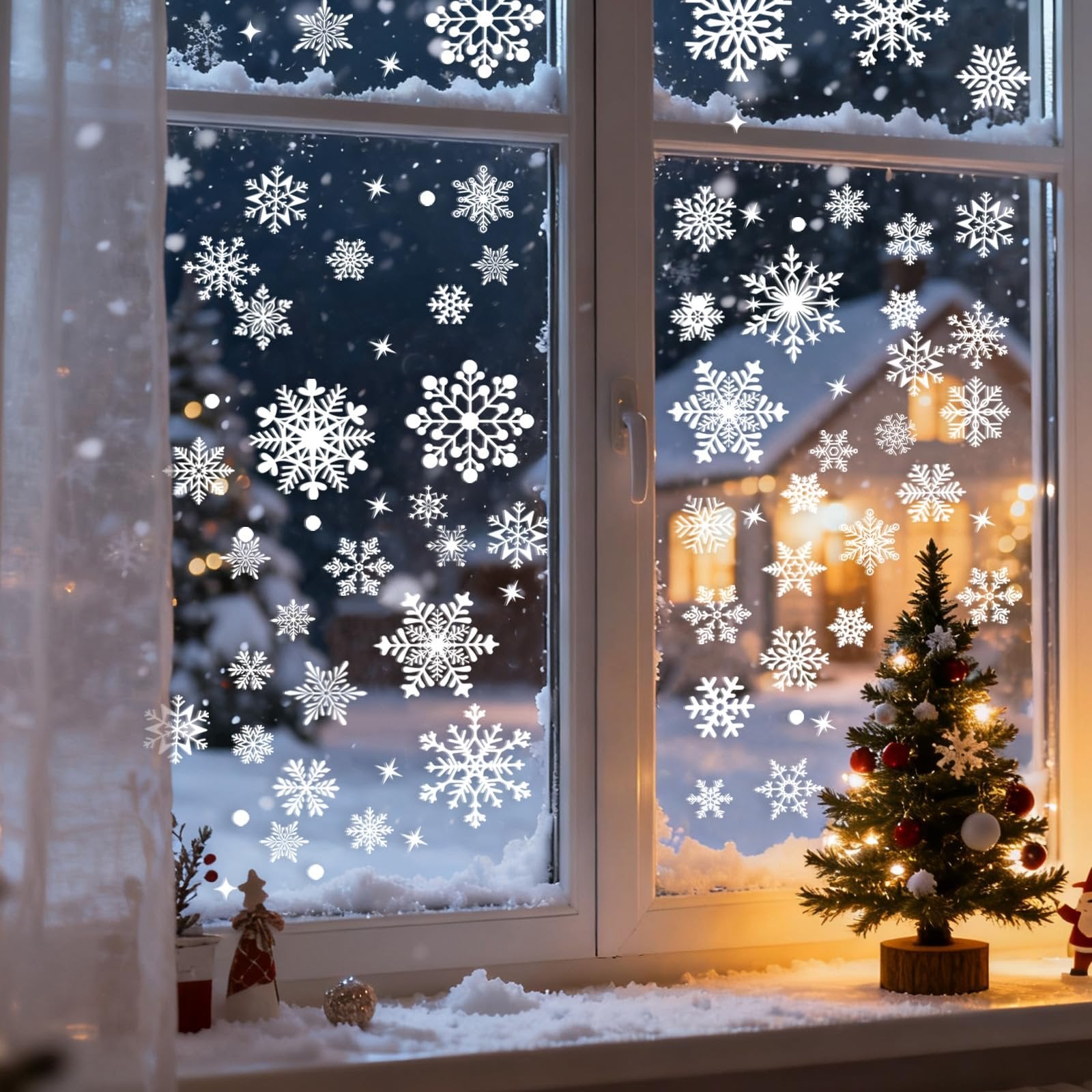 Christmas window decorated with white snowflake clings, showing a snowy scene outside with a decorated tree and house lights.