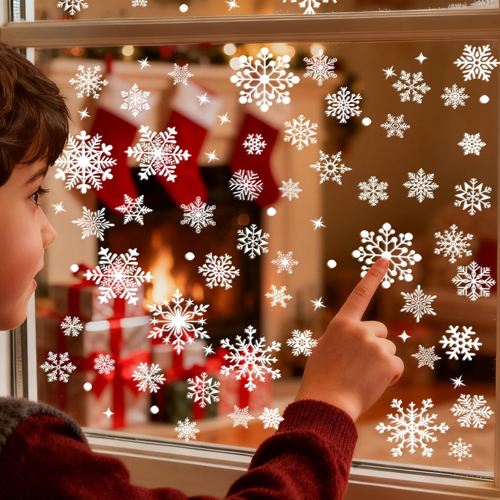 Child's hand pointing at white snowflake window clings on a window with a Christmas fireplace scene in the background.