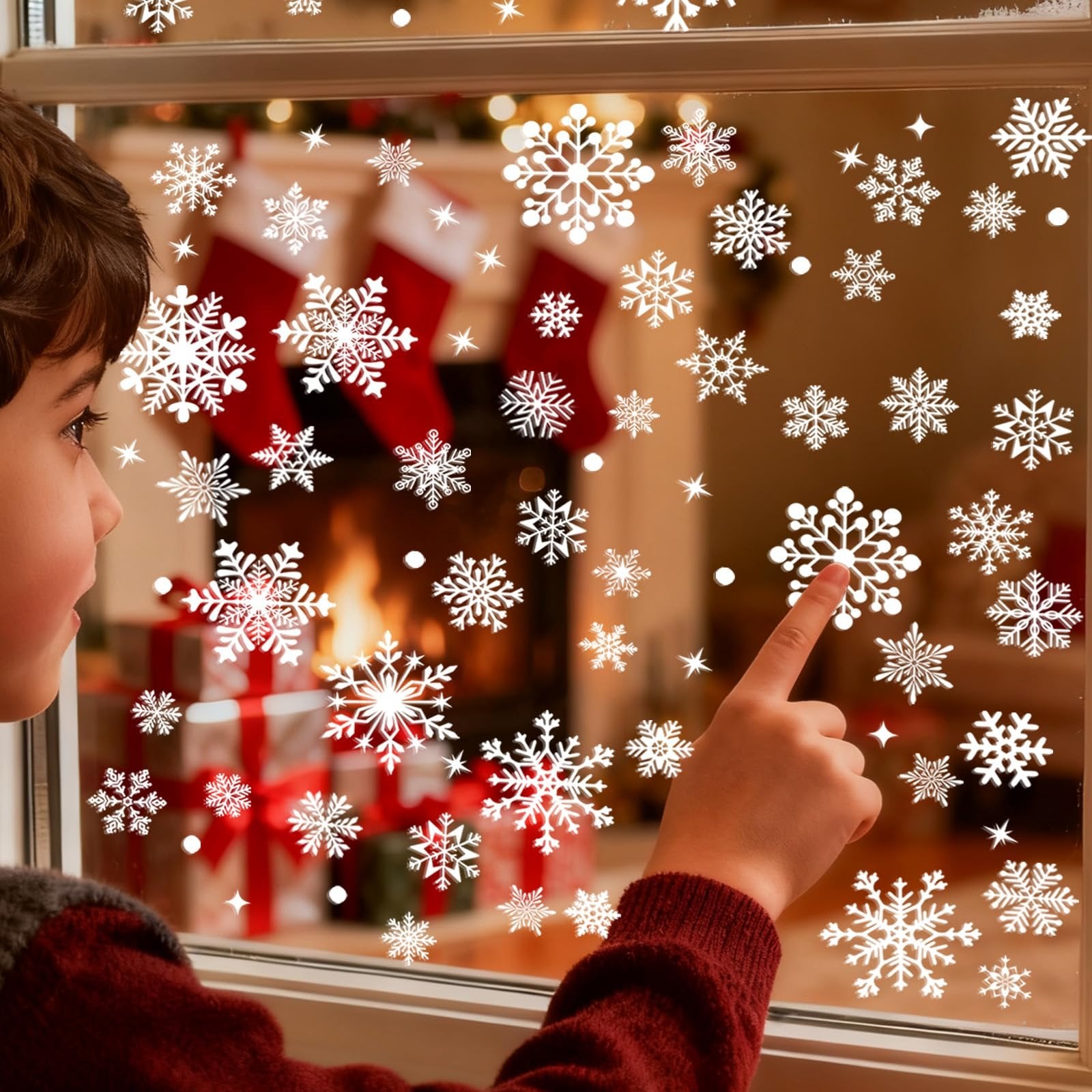 Child's hand pointing at white snowflake window clings on a window with a Christmas fireplace scene in the background.