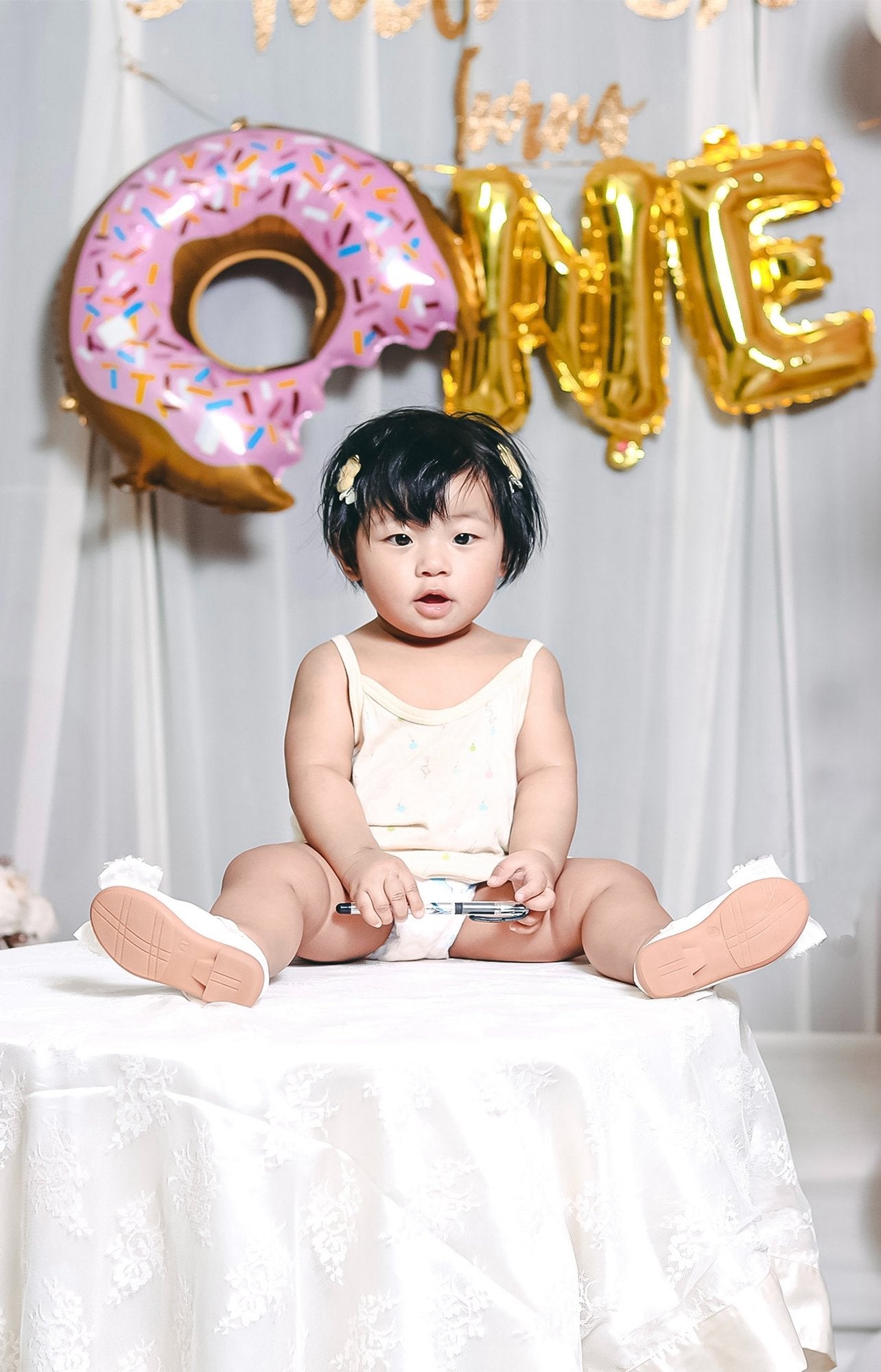 Baby girl sitting on a table with a donut balloon and gold foil letter balloons spelling 'ONE' behind her.