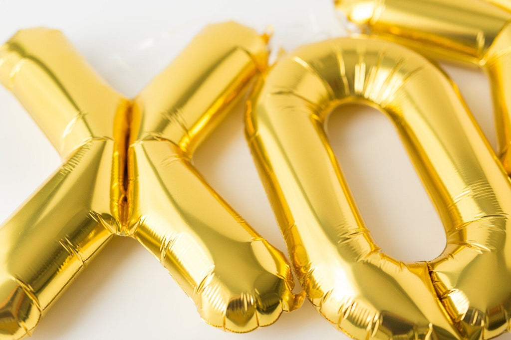 Close-up of gold foil letter balloons spelling XO on a white background.