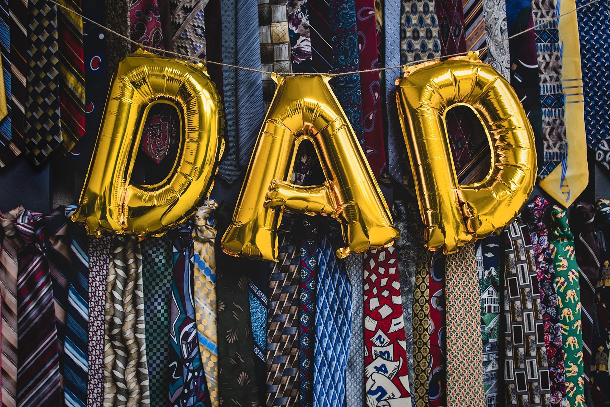 Gold foil letter balloons spelling DAD strung across a backdrop of assorted neckties.