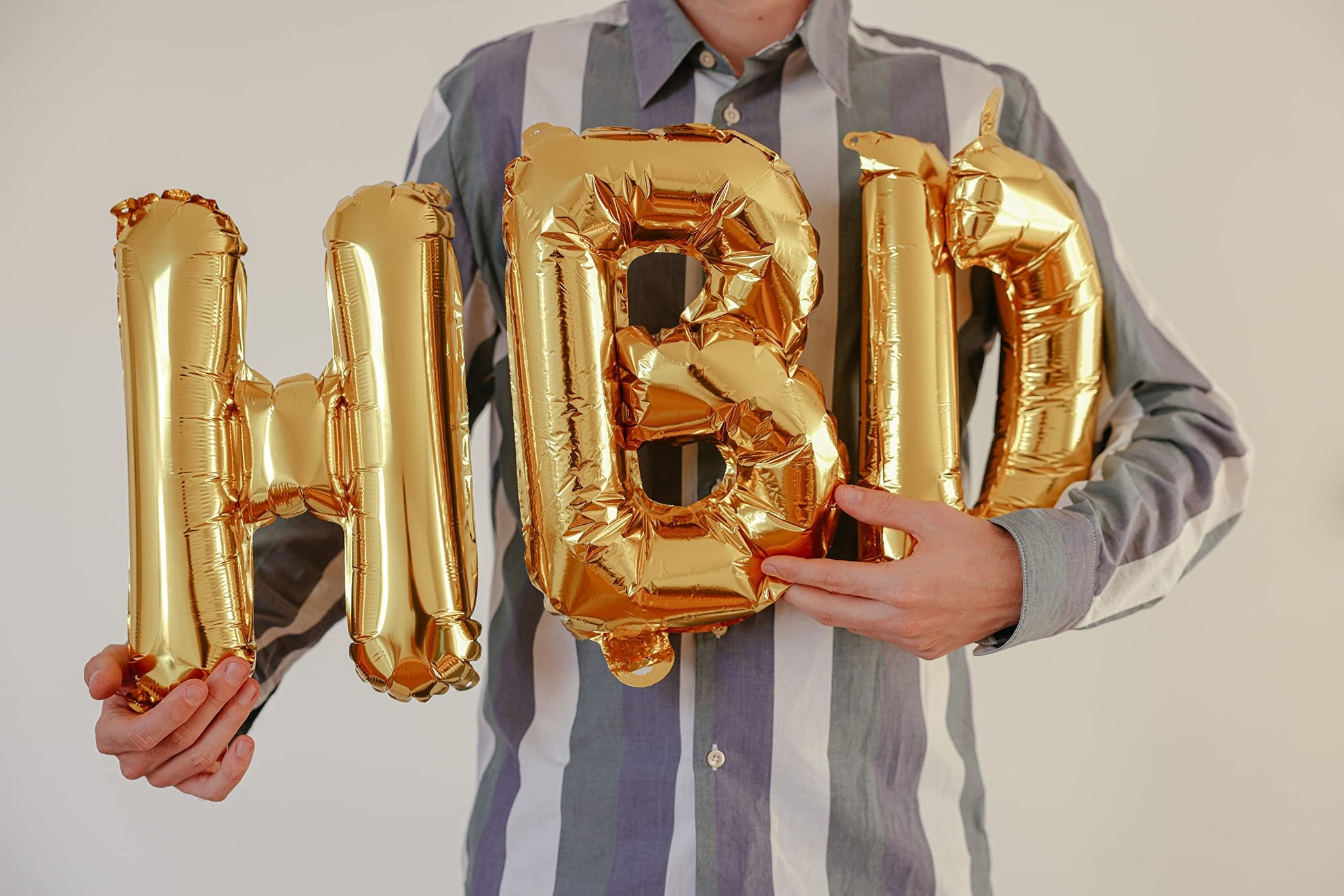 Person holding gold foil letter balloons spelling 'HBD'