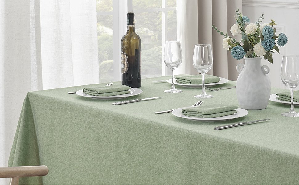 Sage green linen textured tablecloth set for dining with place settings and wine bottle