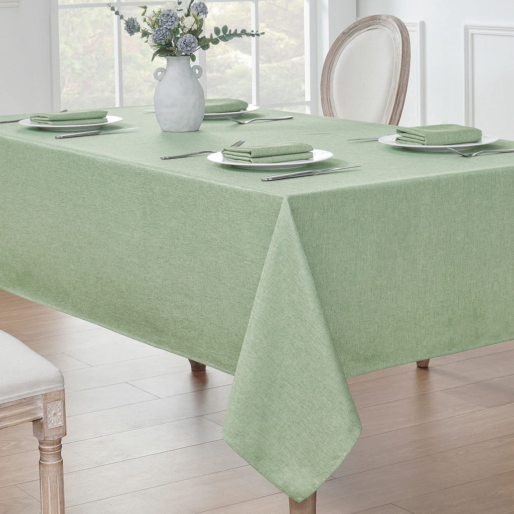Sage green linen textured tablecloth draped over a dining table with place settings and a vase of flowers.