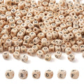 Natural wood cube alphabet beads scattered and displayed in rows, showing various letters printed on each side.