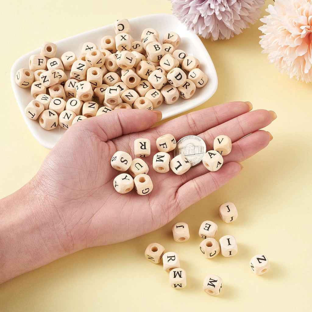 Hand holding natural wood cube alphabet beads with letters printed on them, with more beads in a white dish and scattered around.