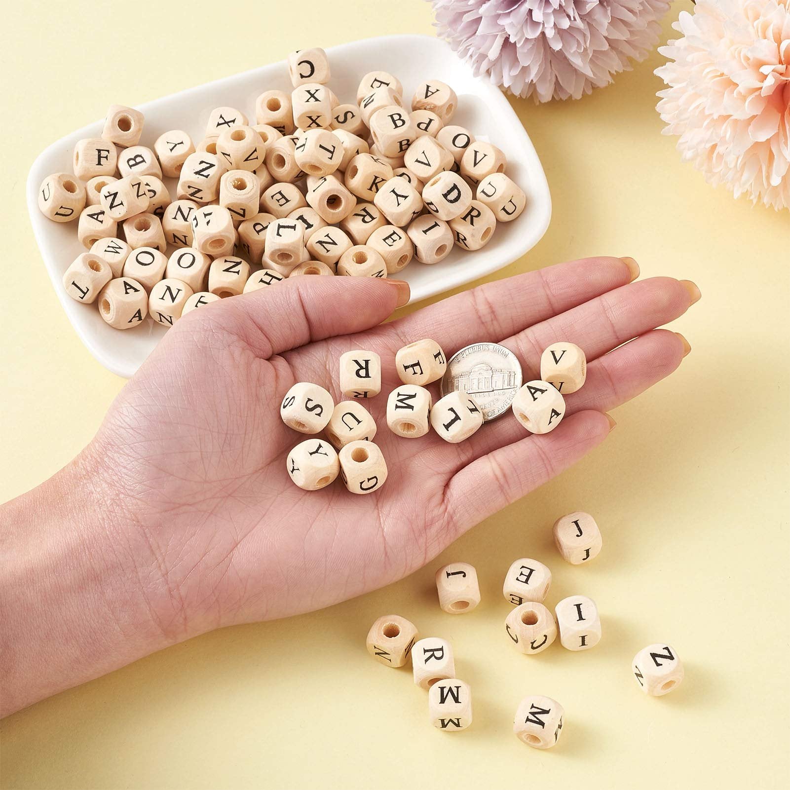 Hand holding natural wood cube alphabet beads with letters printed on them, with more beads in a white dish and scattered around.