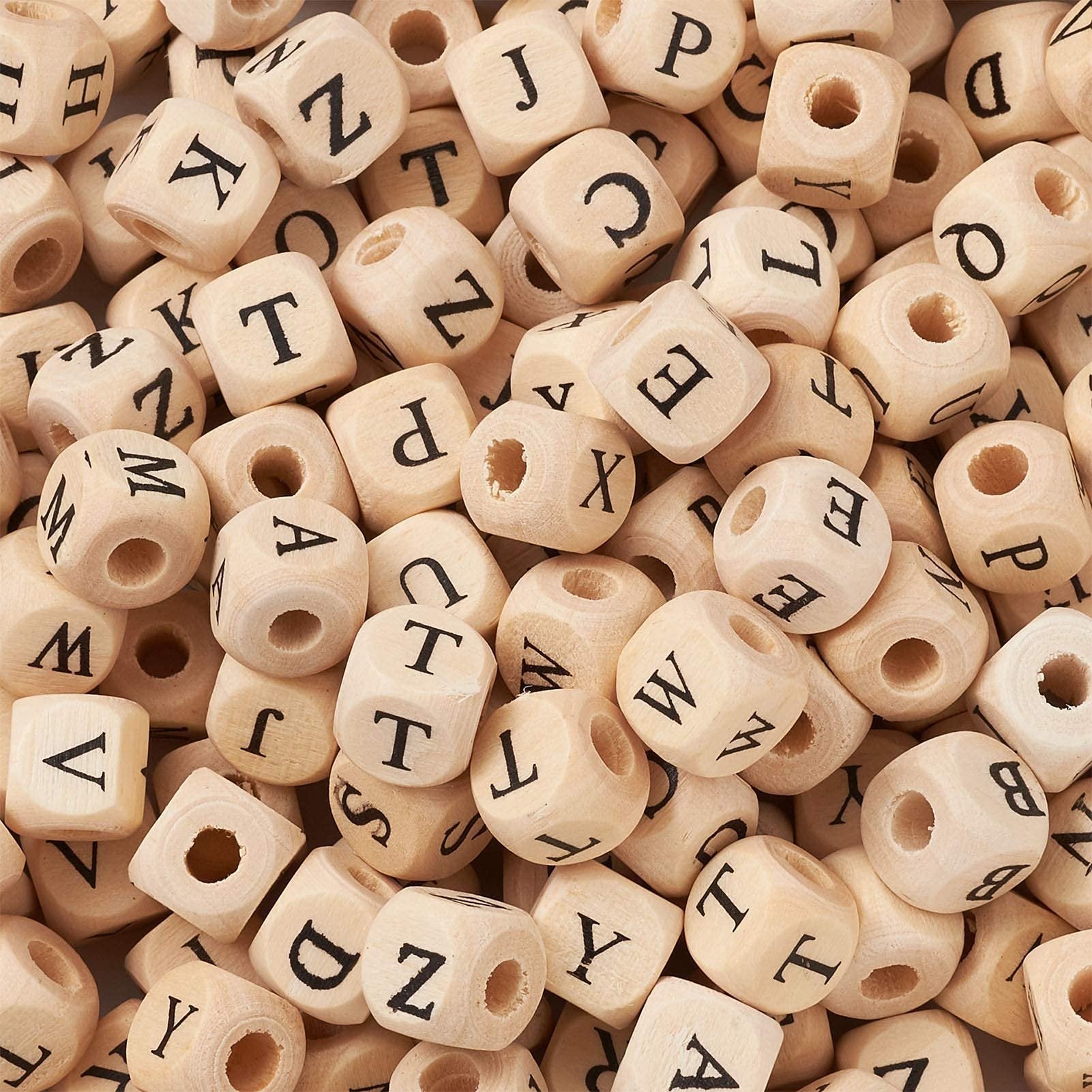 Pile of natural wood cube alphabet beads with black letters, close-up view.