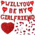Red heart and letter balloons spelling 'Will You Be My Girlfriend' with rose petals and a heart-shaped pile of petals.