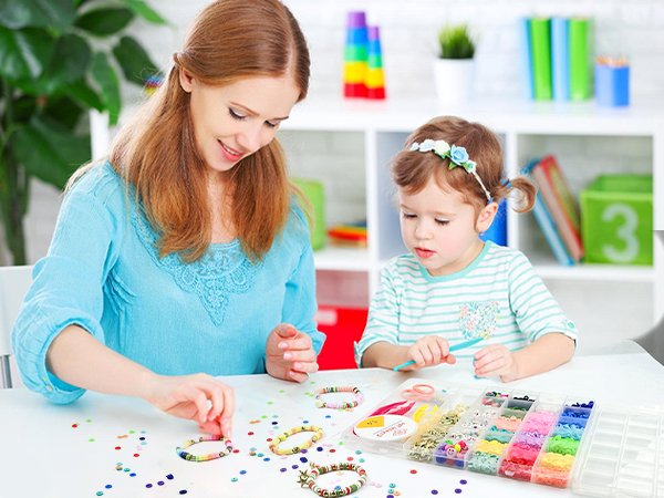 Mother and daughter making bracelets with a large assortment of colorful beads and charms in a clear organizer case.