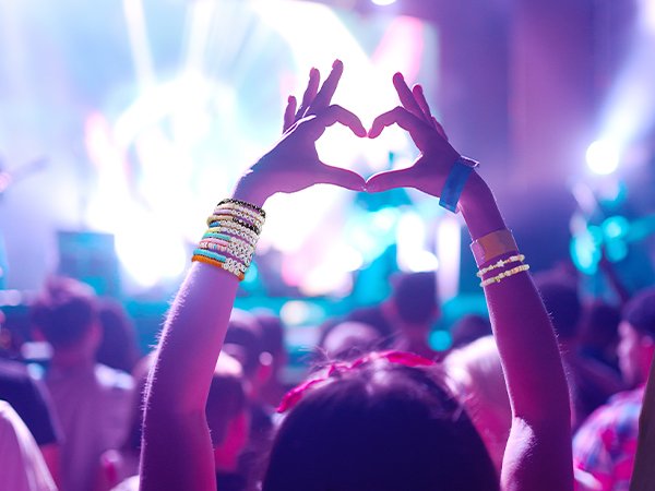 Hands forming a heart shape at a concert, wearing colorful beaded bracelets.