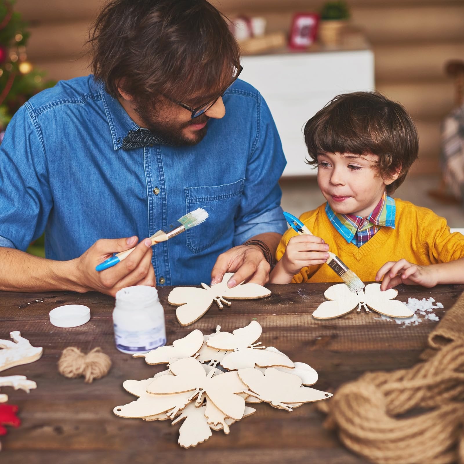 Father and son painting unfinished wooden butterfly cutouts on a wooden table, with craft supplies nearby.