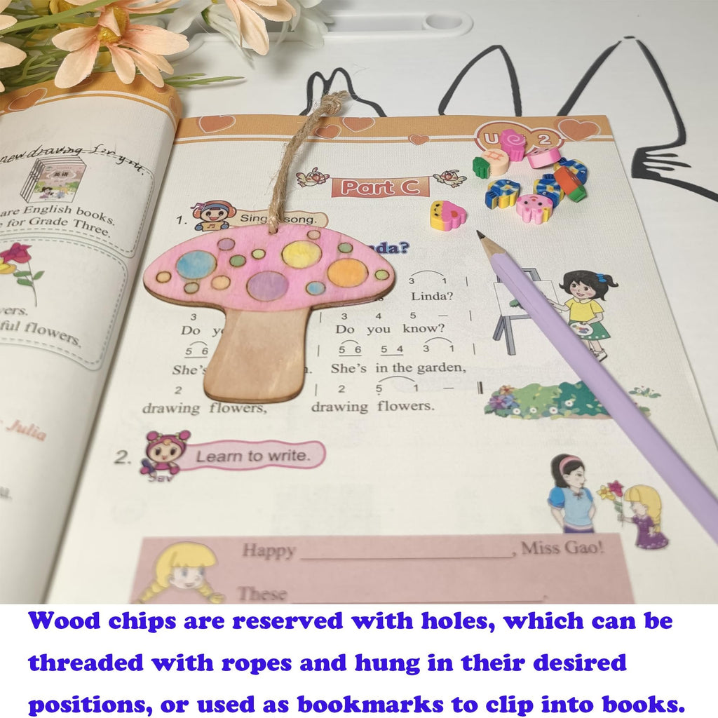 A wooden mushroom cutout with pink and yellow polka dots hangs from a book page with a hemp rope. A purple pencil rests on the page.