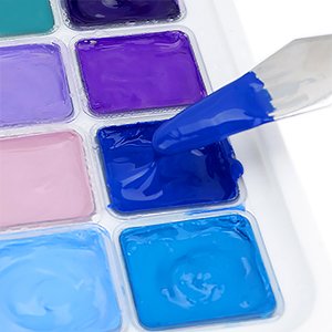 Close-up of a palette of 56 colors of gouache paint in jelly cups, with a spatula scooping blue paint.