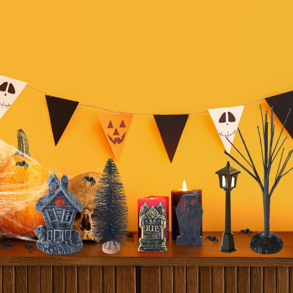 Halloween village accessories including a haunted house, skull, pumpkin, trees, candles, and streetlamp on a shelf with a festive banner overhead.