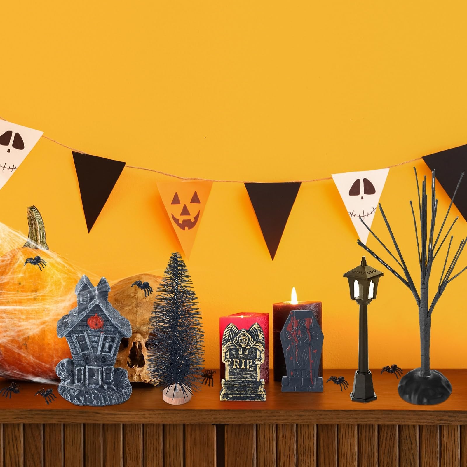 Halloween village accessories including a haunted house, skull, pumpkin, trees, candles, and streetlamp on a shelf with a festive banner overhead.