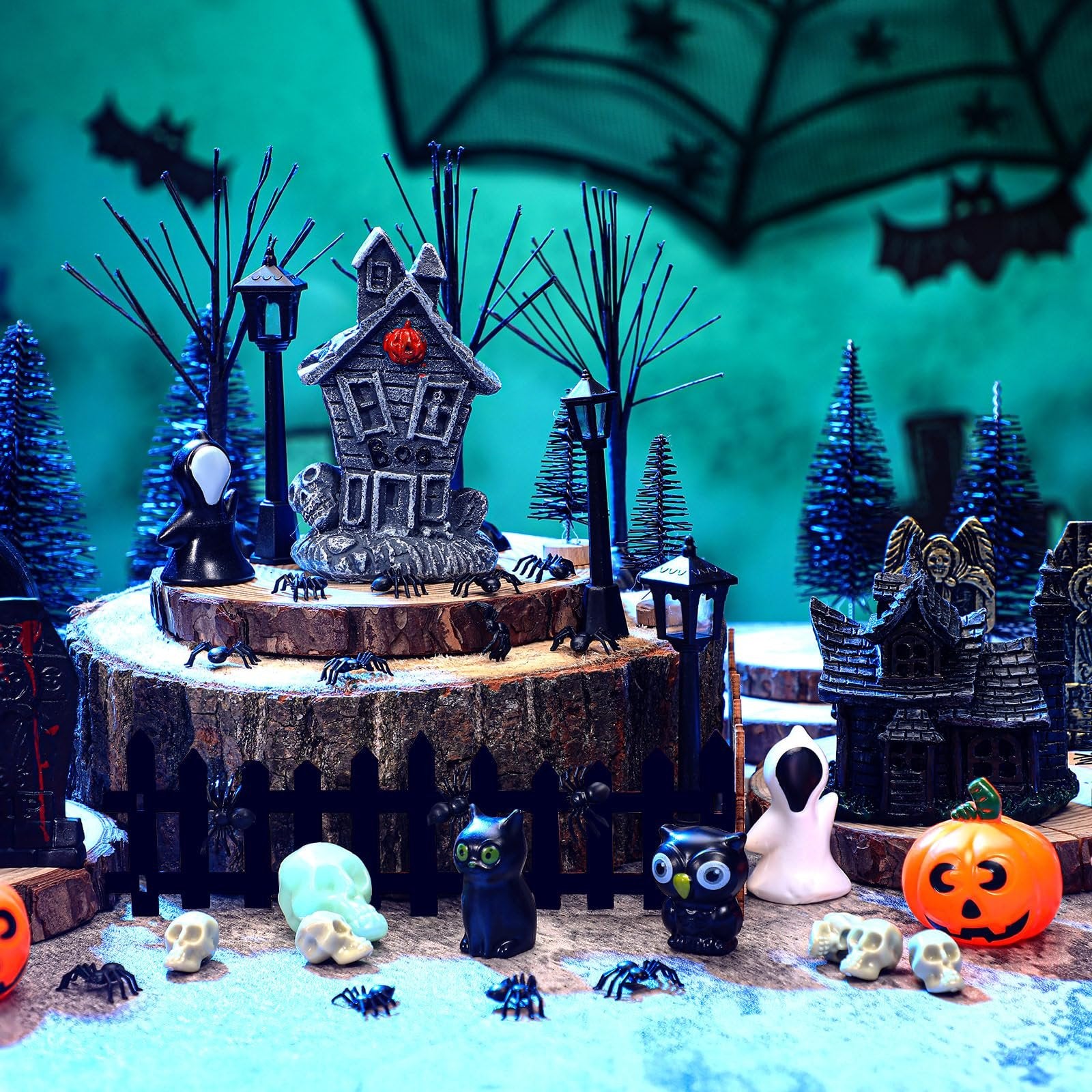 Halloween village accessories including haunted houses, tombstones, trees, fence, streetlamps, spiders, skulls, a black cat, an owl, a ghost figure, and a jack-o'-lantern.