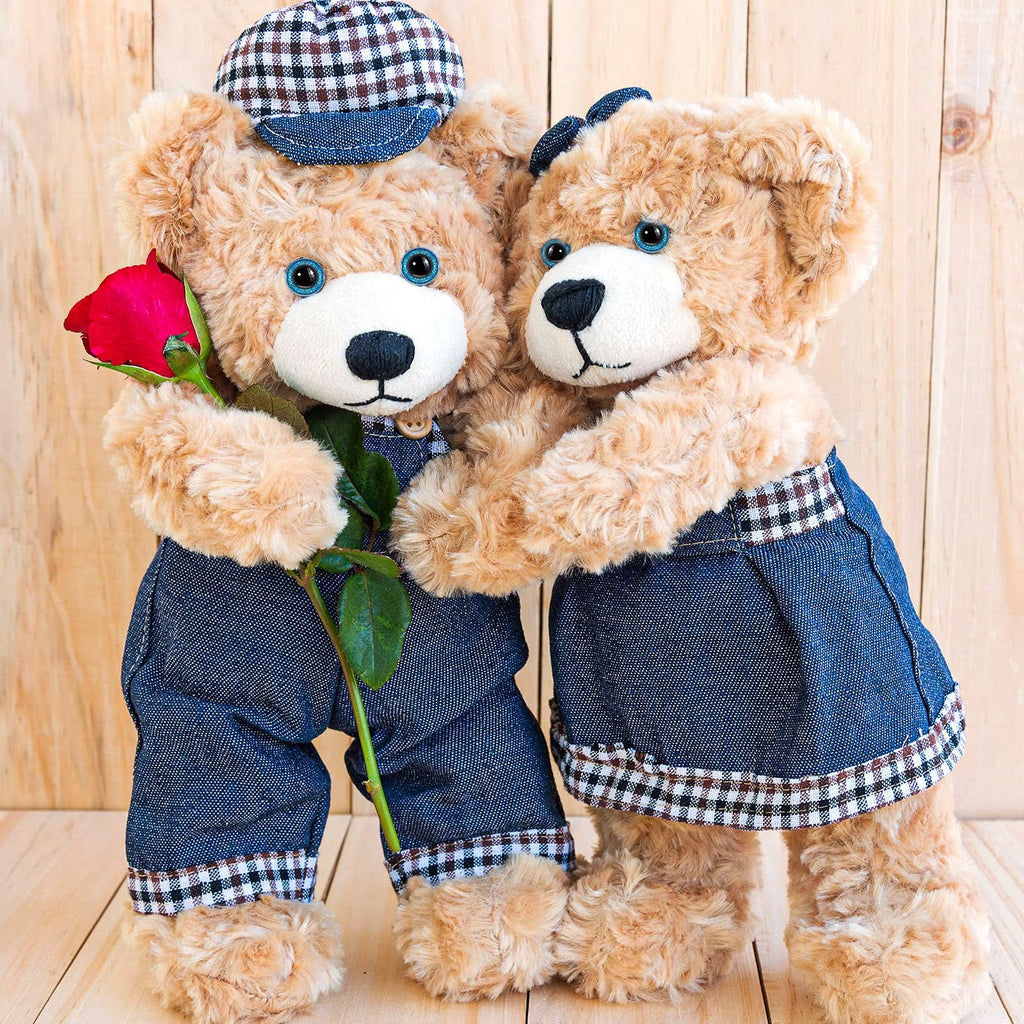 Two teddy bears in denim outfits, one holding a red rose, against a wooden background.