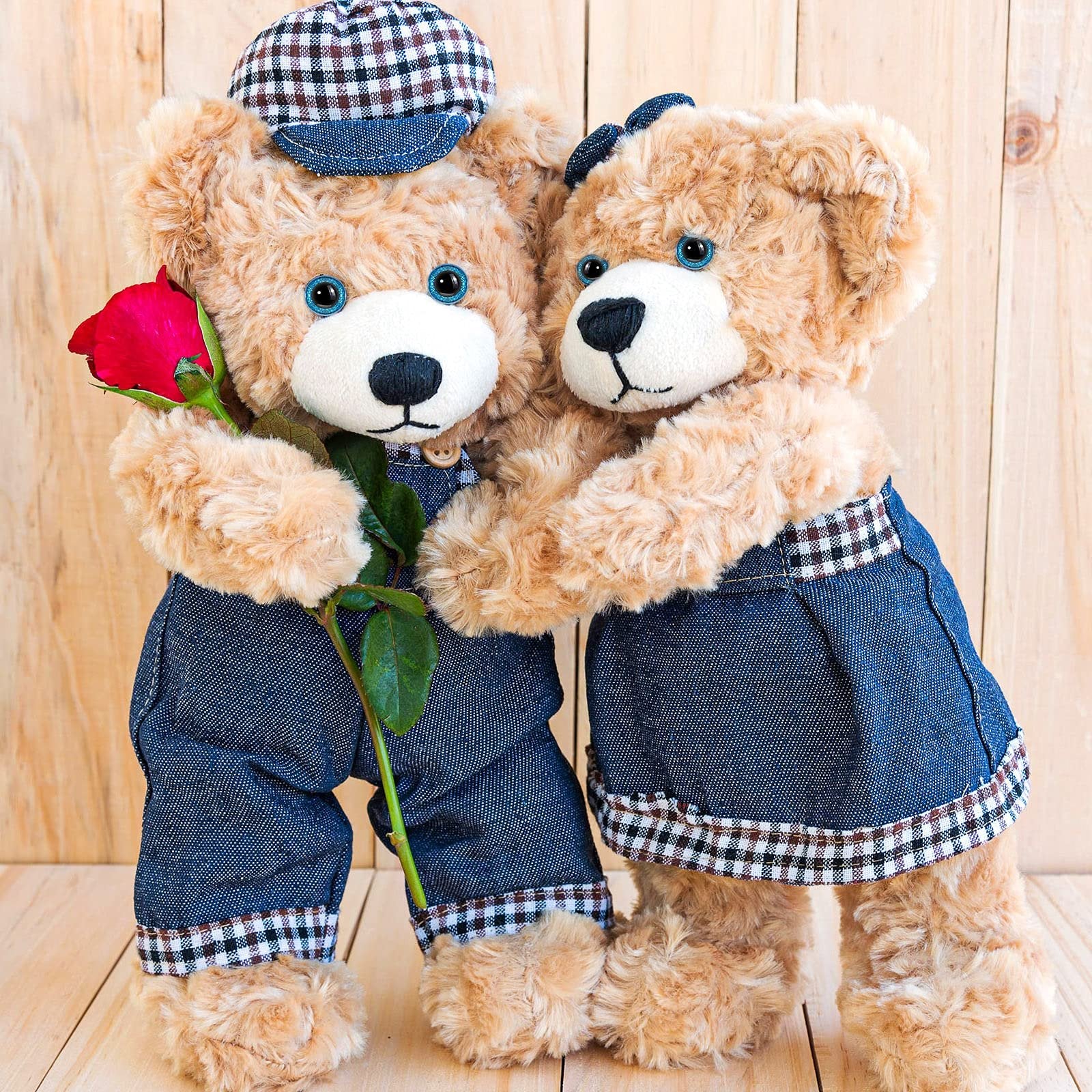 Two teddy bears in denim outfits, one holding a red rose, against a wooden background.