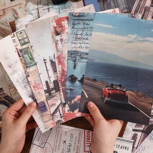 Hands holding a fan of vintage travel-themed scrapbook paper sheets with scenic and postcard designs.