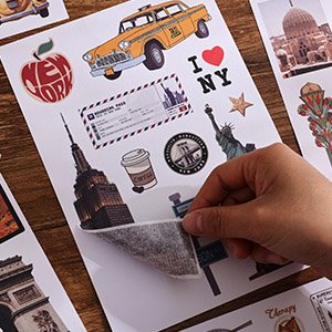 Hand peeling a sheet of vintage travel stickers featuring New York City landmarks, taxi, and apple.