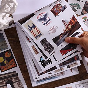 Stack of vintage travel-themed scrapbook sticker sheets held by a hand, featuring landmarks and retro designs.