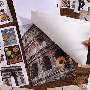 Close-up of vintage travel scrapbook stickers featuring the Colosseum, Eiffel Tower, and Paris landmarks, with a hand peeling back a sheet.