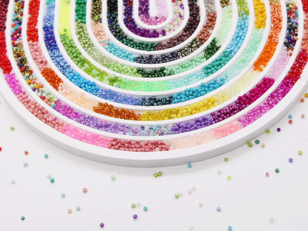 Close-up of a white organizer tray filled with colorful glass seed beads arranged in concentric arcs on a white background.