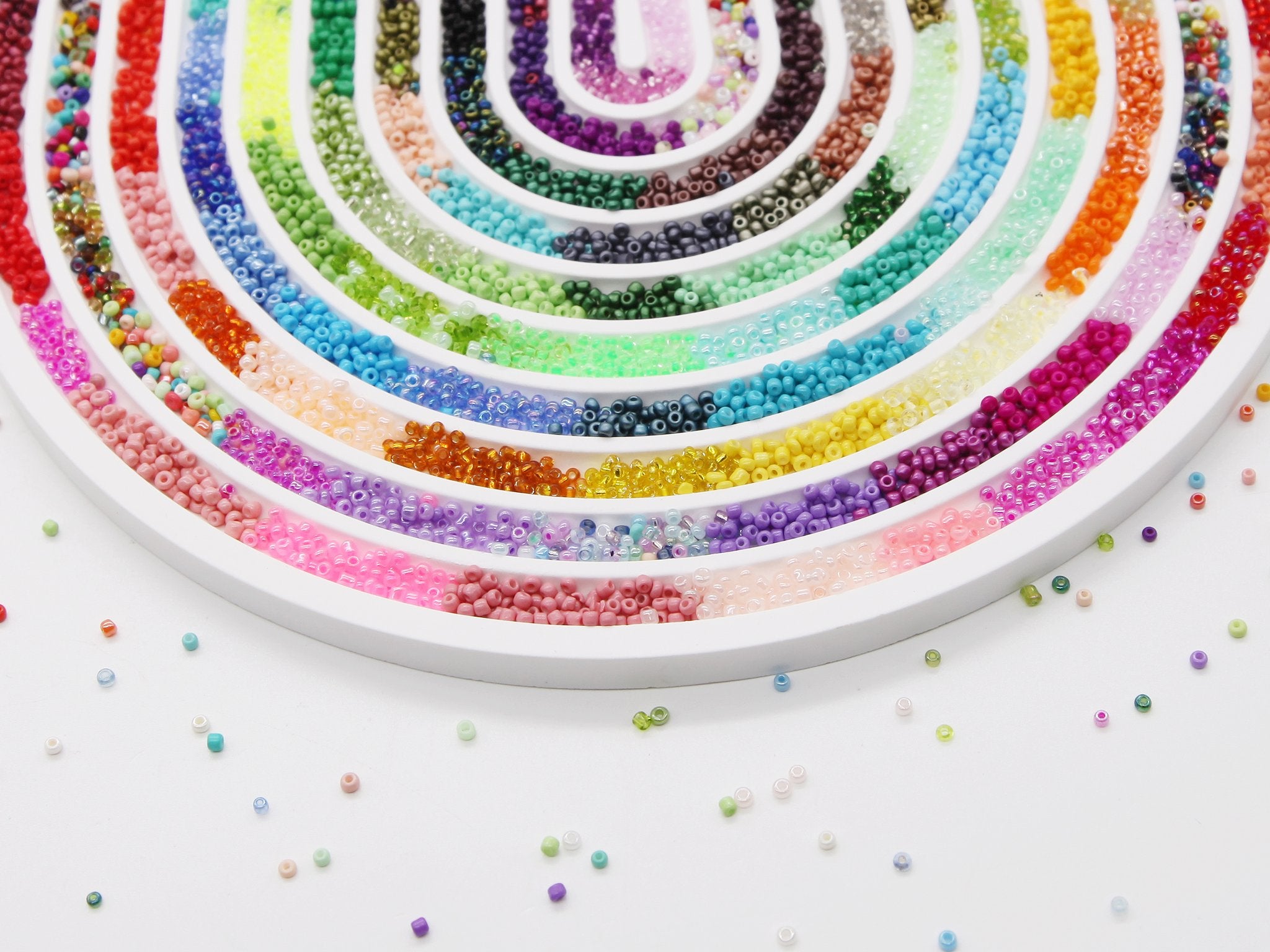 Close-up of a white organizer tray filled with colorful glass seed beads arranged in concentric arcs on a white background.