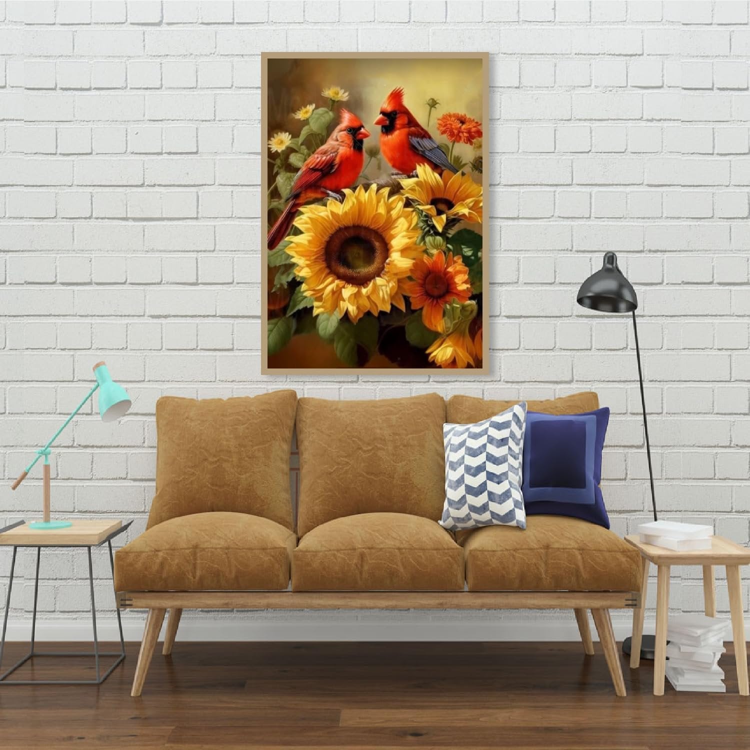 Two cardinals perched on sunflowers in a framed artwork displayed on a white brick wall above a sofa.