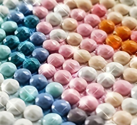 Close-up of colorful diamond painting beads arranged in rows, showing a gradient of blues, greens, pinks, and oranges with sparkling highlights.