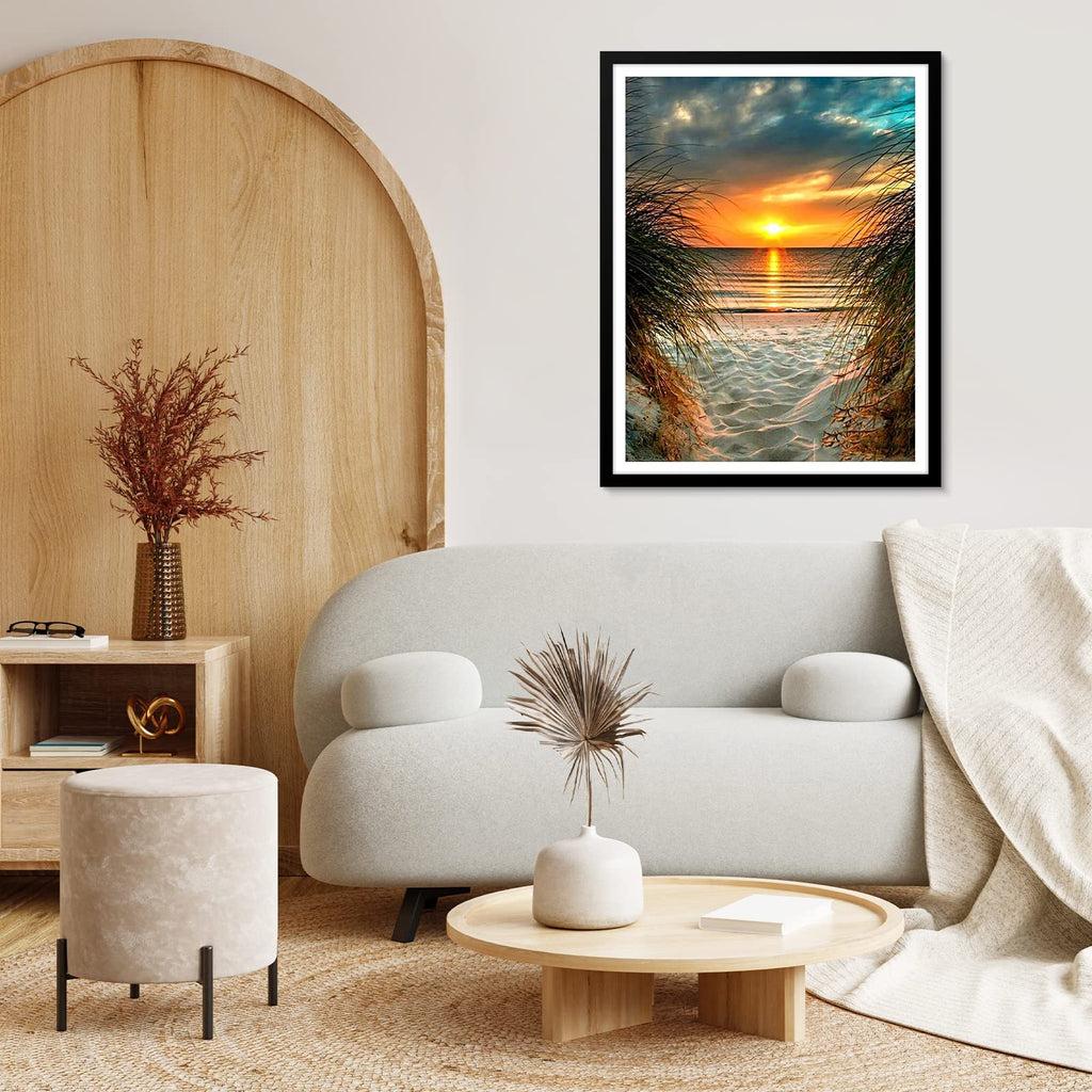 Framed diamond painting of a beach sunset viewed through tall grass, displayed in a living room setting.