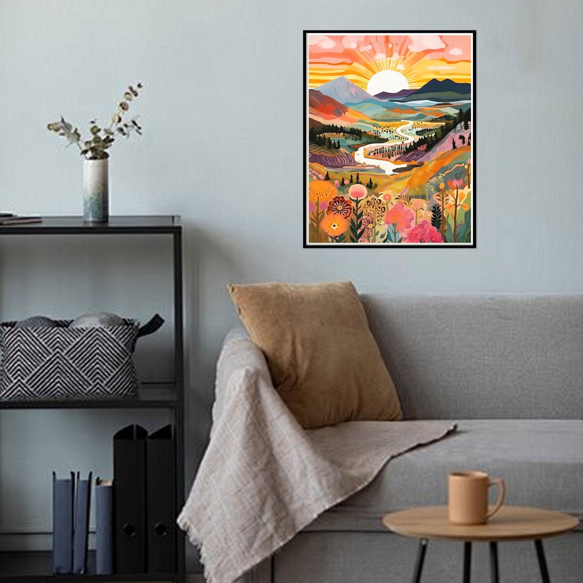 Framed abstract sunrise landscape painting with mountains and flowers hanging on a wall above a sofa.