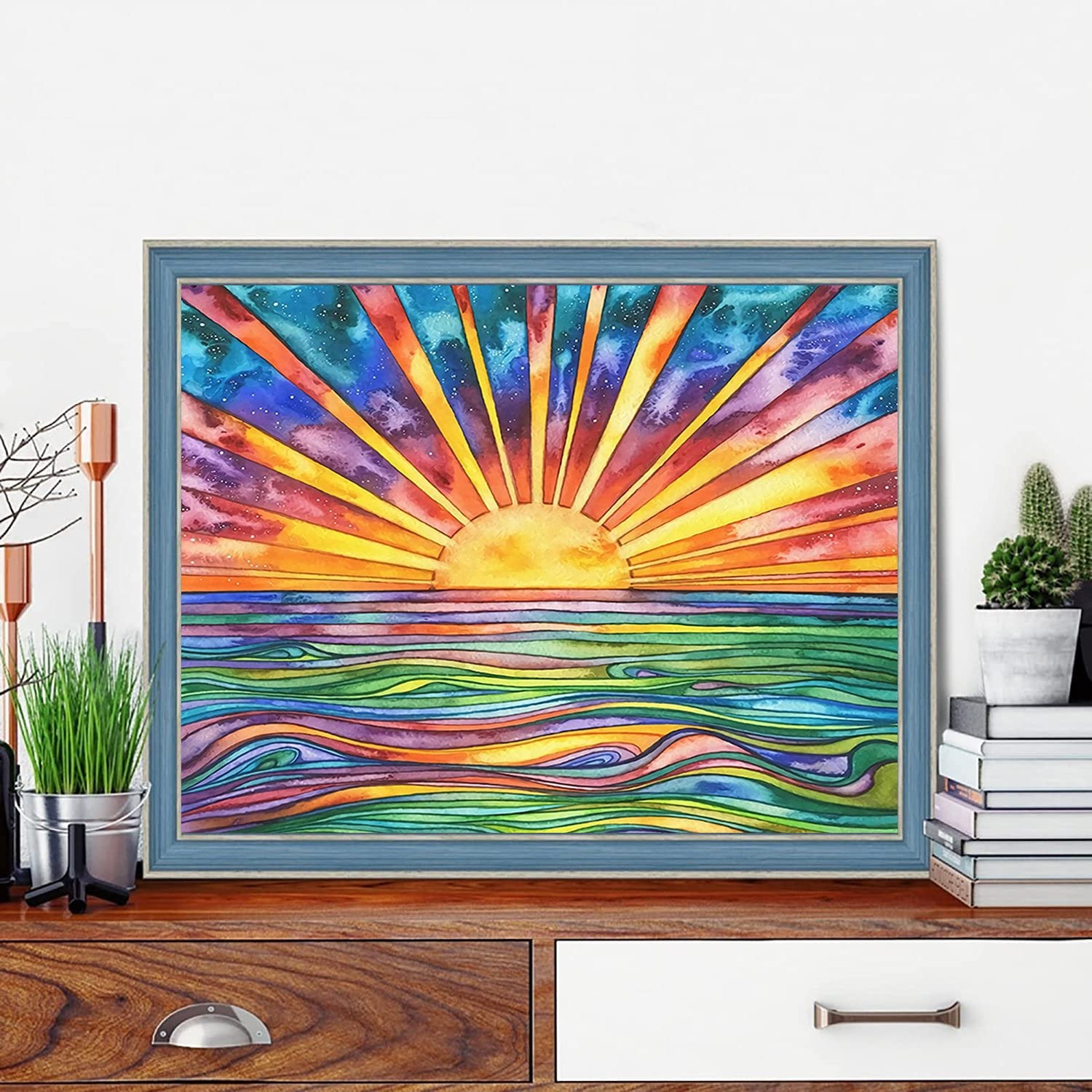 Framed abstract sunrise over colorful wavy ocean, displayed on a wooden dresser with plants and books.