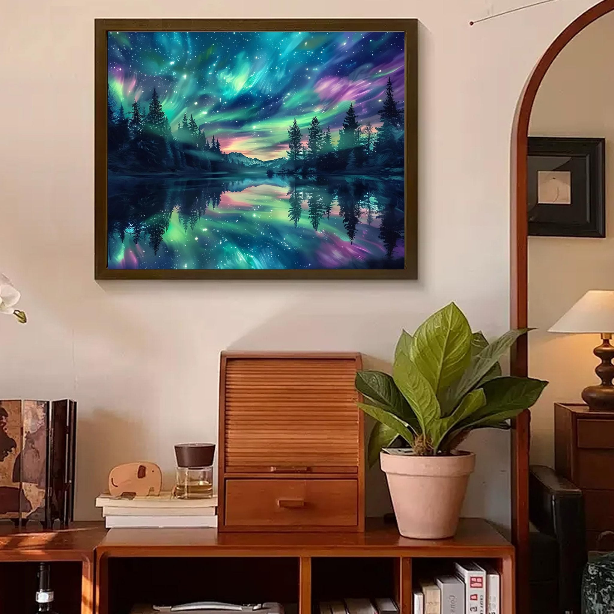 Framed diamond painting of a starry night sky with aurora borealis over a forest and lake, displayed on a wall above furniture.