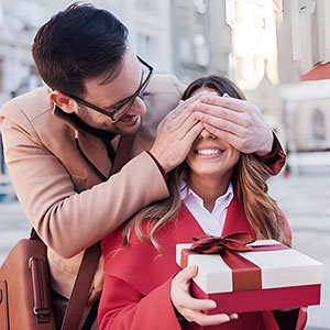 Man surprising woman with a gift box, covering her eyes with his hands