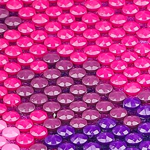 Close-up of a diamond painting kit with pink and purple faceted beads arranged in a pattern.