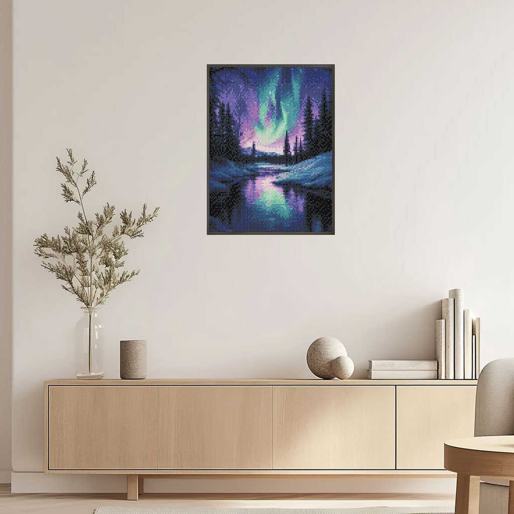 Diamond painting of the Aurora Borealis over a snowy forest and lake, framed and hung on a wall.