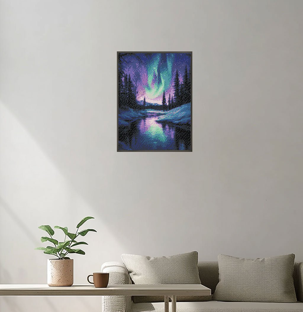 Diamond painting of the Aurora Borealis over a reflective lake and pine trees, framed and hanging on a wall.