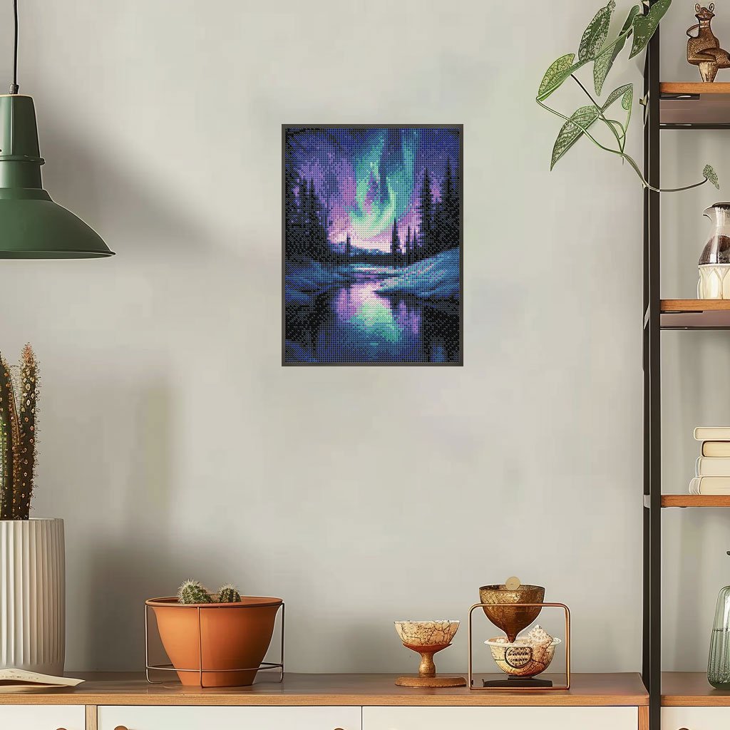 Diamond painting of Aurora Borealis over a snowy landscape and reflective water, framed and hung on a wall.