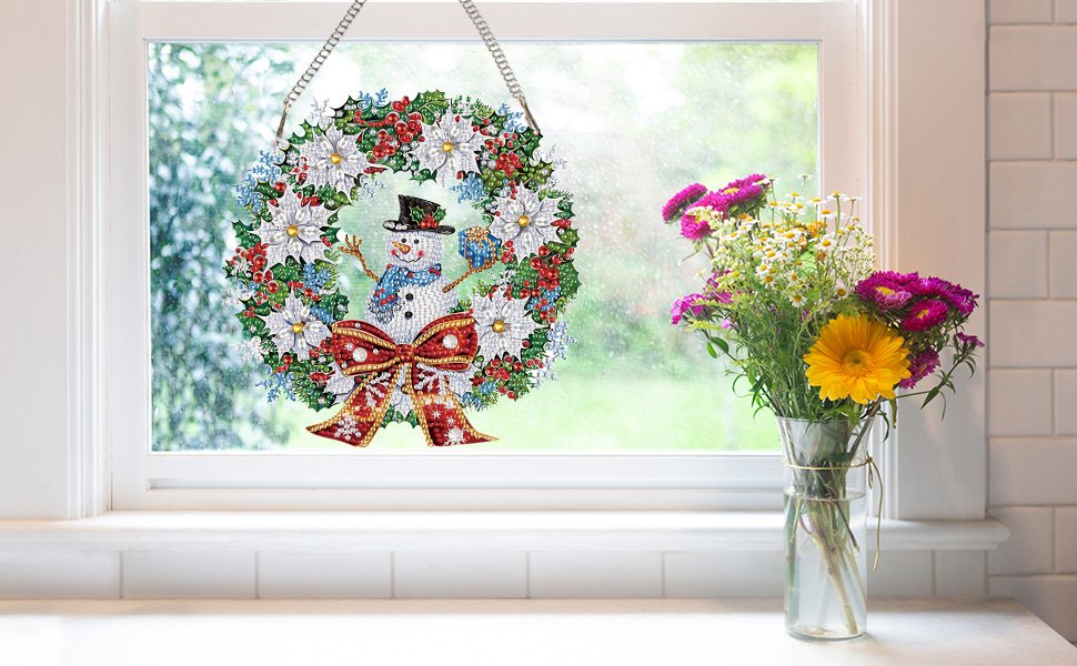 Diamond painting snowman wreath ornament hanging on a window with a bow and flowers in a vase nearby