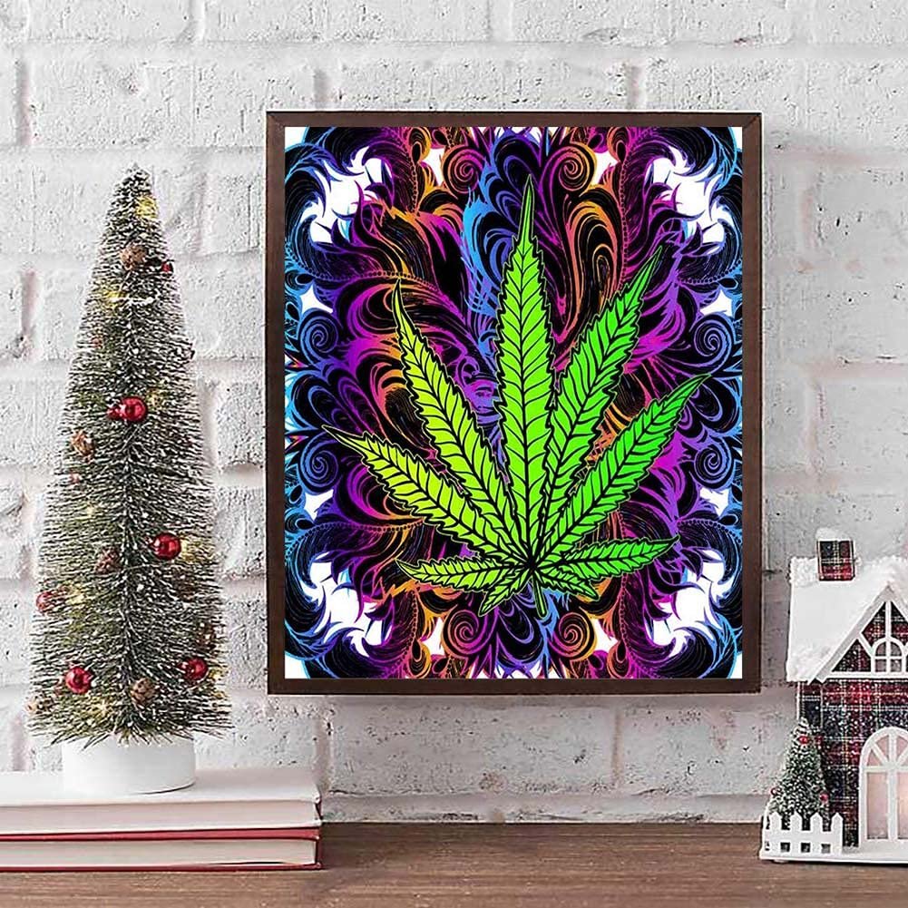 Framed diamond art painting of a green cannabis leaf with a colorful, swirling background, displayed on a shelf.