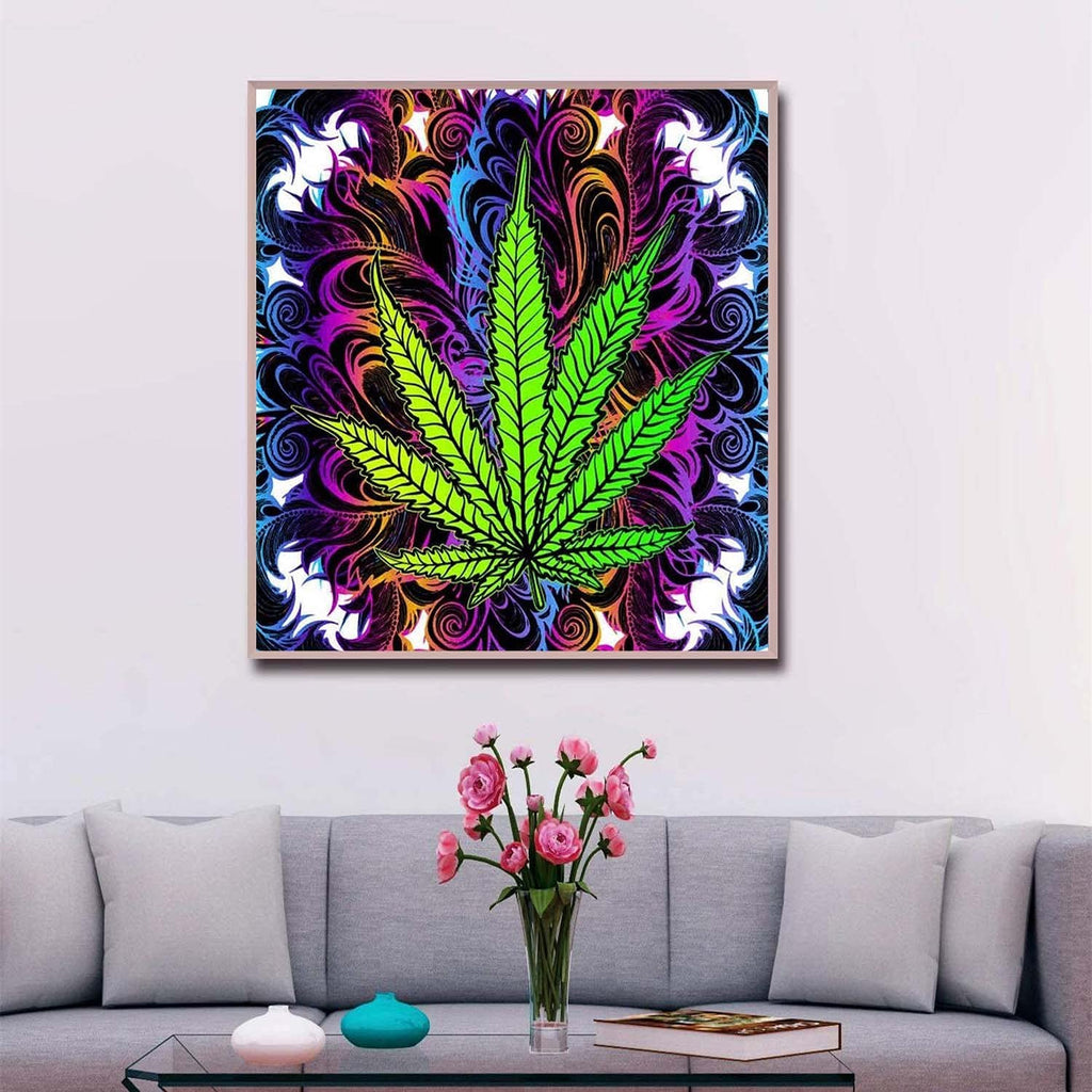 Framed 5D DIY diamond art painting of a green cannabis leaf with a colorful, swirling background, displayed on a wall above a sofa.