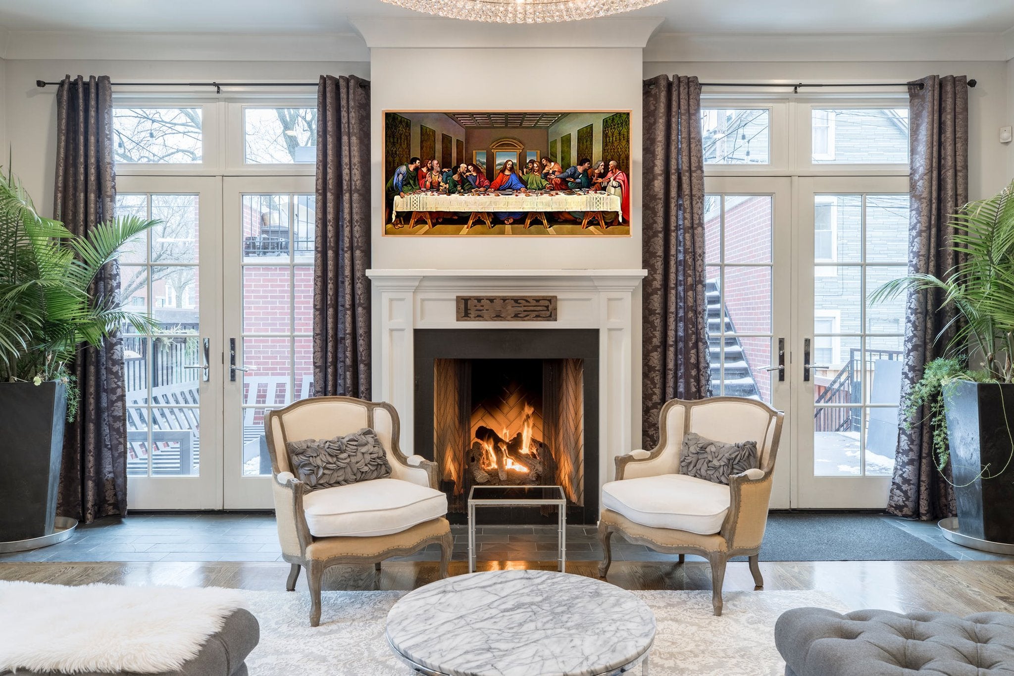 Living room with a framed painting of The Last Supper above a fireplace, flanked by chairs and plants.