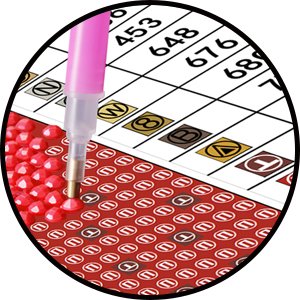 Close-up of diamond painting kit showing a pink tool placing a red rhinestone onto a numbered grid, with chart of numbers in background.