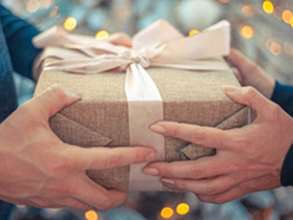 Two people exchanging a wrapped gift with a pink ribbon and bow, bokeh lights in background